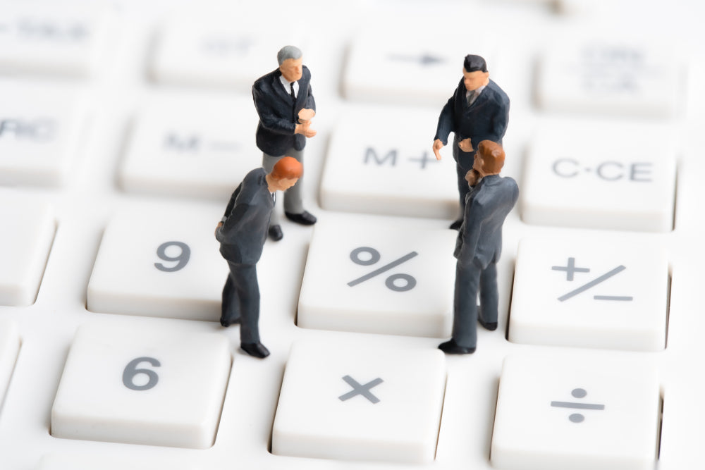 Miniature business figures standing on a calculator keyboard, symbolizing financial discussions, calculations, or business strategies.
