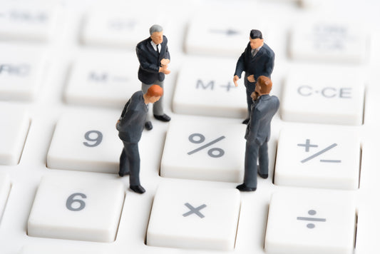 Miniature business figures standing on a calculator keyboard, symbolizing financial discussions, calculations, or business strategies.