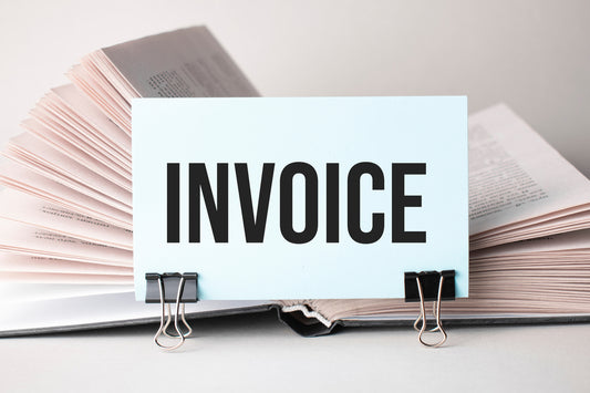 An open book with a card labeled "INVOICE" clipped to the pages, symbolizing financial documents or billing processes.