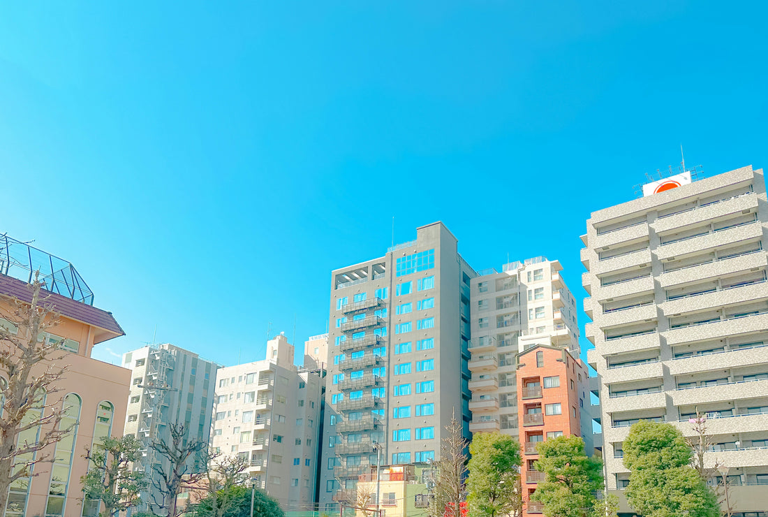 A row of modern office and residential buildings in Tokyo under a clear blue sky, surrounded by trees and urban scenery.