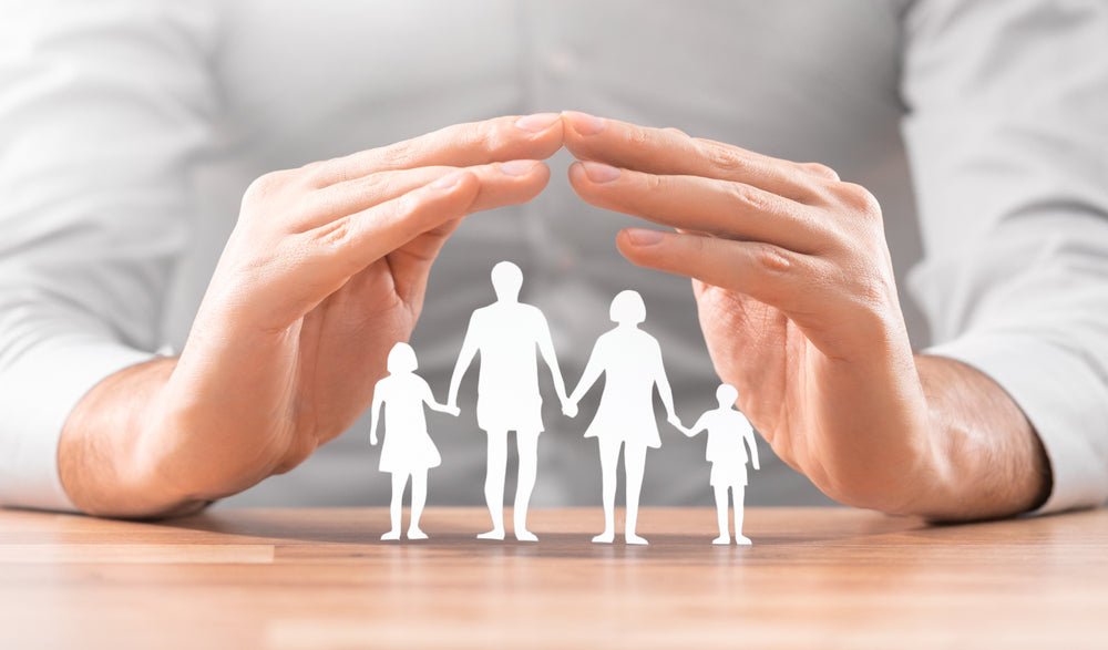 Hands forming a protective gesture over a paper-cut family figure symbolizing safety, security, and family care.