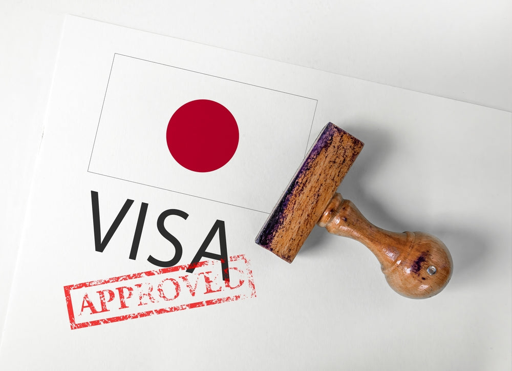 Japanese visa application stamped 'Approved' with a wooden rubber stamp placed on a document featuring the Japanese flag.